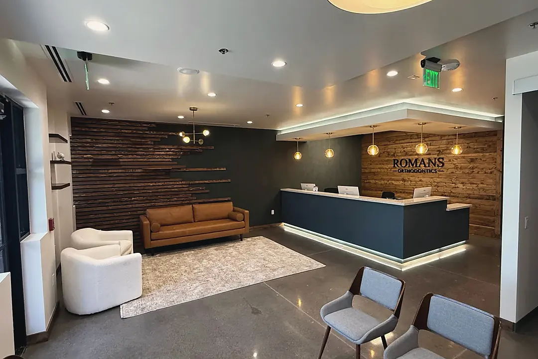 The reception area at Romans Orthodontics: wood-slat wall, lit front desk under the practice sign, and seating for waiting families